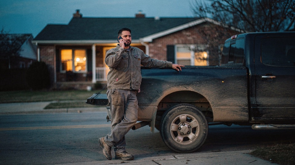 A contractor beside his truck at dusk, taking a call he already knows was handled.